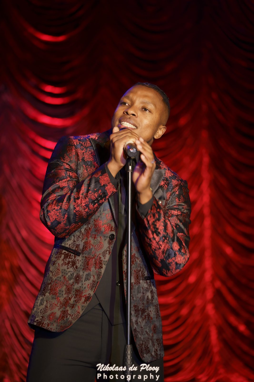 Thuba Myeki at the microphone against a red curtain